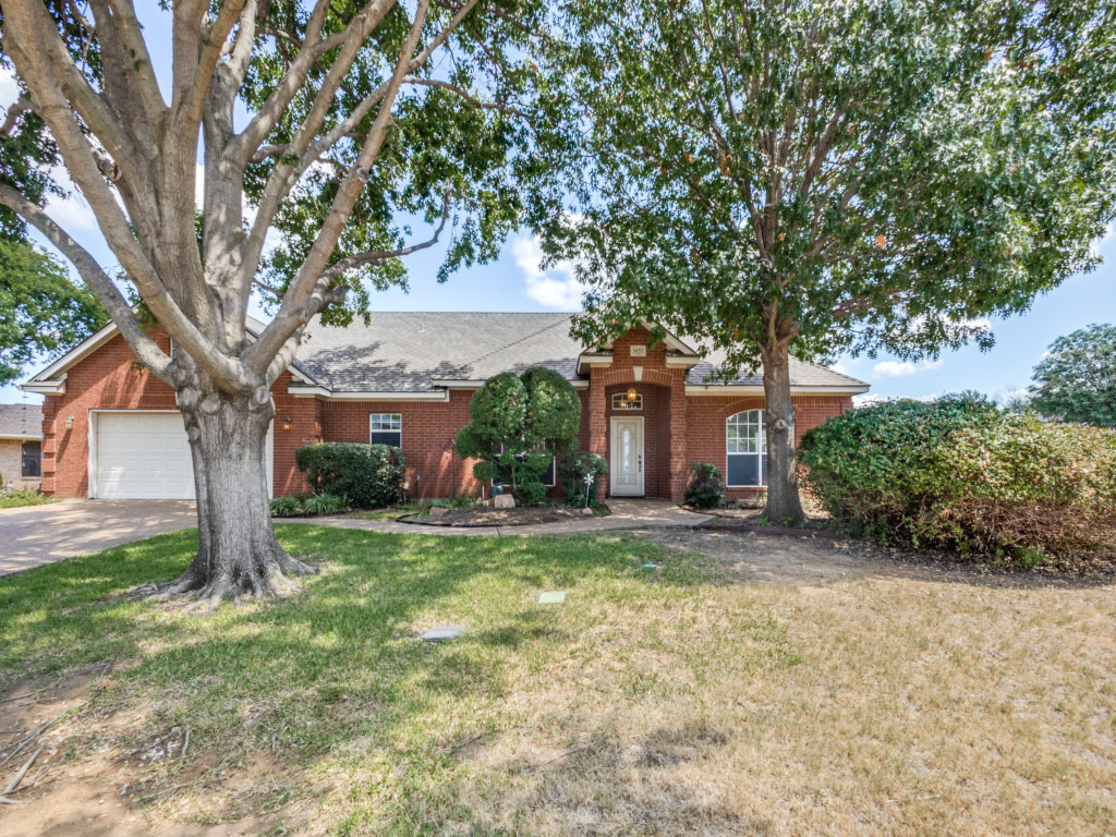 Front view of a charming single-story home on a corner lot in Flower Mound, featuring a well-manicured lawn, mature trees, and a welcoming entrance.